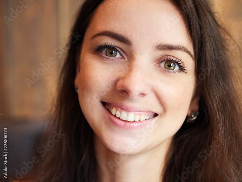 Big close up portrait of beautiful cute brunette girl in the cozy cafe near the window with shy smiling