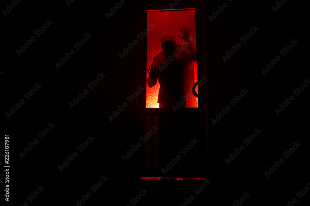 Silhouette of an unknown shadow figure on a door through a closed glass