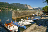 Barche ancorate in un piccolo porto di lago con montagne sullo sfondo e cielo blu in estate, Isola dei Pescatori, Lago Maggiore, Italia