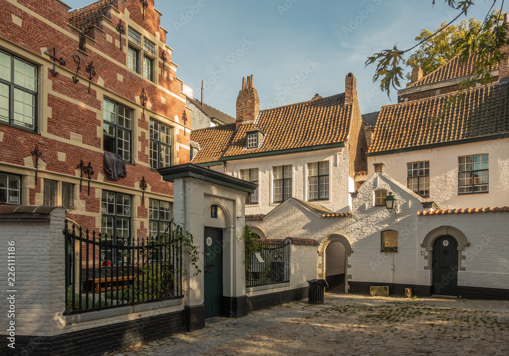 Fototapeta premium Kortrijk, Flanders, Belgium - September 17, 2018: Twilight falls on corner of the beguinage with white and red brick housing. Gray courtyard. Some green foliage.