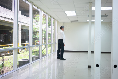 Businessman standing in empty bright office and look at wall thinking