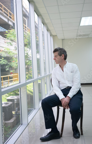 Businessman sitting in old chair in empty bright office and look out the window thinking