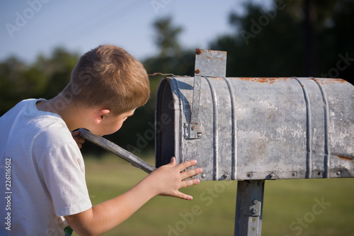 A cute boy, checking the mail in an open mail box. The kid is waiting for the letter, checks the correspondence and looks into the metal mailbox. photo