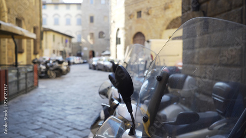 Blurred backdrop of Italian cobblestone street with cars and mopeds parked