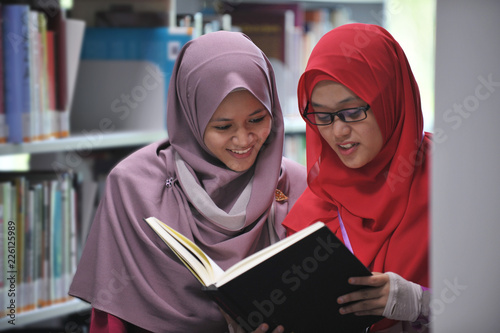 Two young beautiful muslimah student discussing in the library.