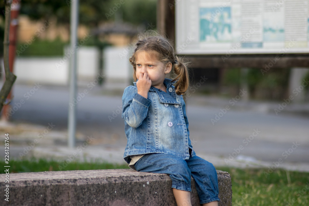 little girl sitting on a bench and picking her nose little girl sitting on a bench and picking her nose