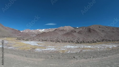 Traveling over gravel road with 4x4 van beside valley of Desaguadero River between high desertic, rocky, coloured, snowy mountains. Excursion to Brava Lagoon at The Andes. Rioja photo