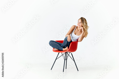 cute blond woman sitting on a red chair on a white isolated background