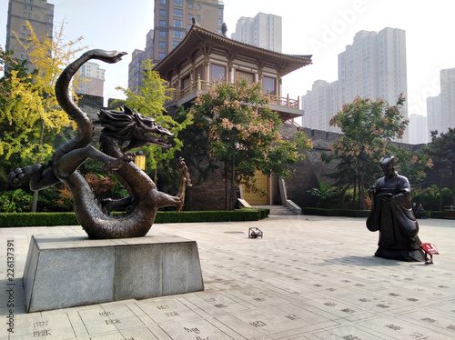 Statue of a man and dragon in front of stylized city wall with blooming trees in spring. Qujiang district, Xian city, Shaanxi province, China. Modern chinese city. photo