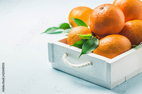 Mandarines and leaves  in a box on light blue background. Selective focus, space for text. photo