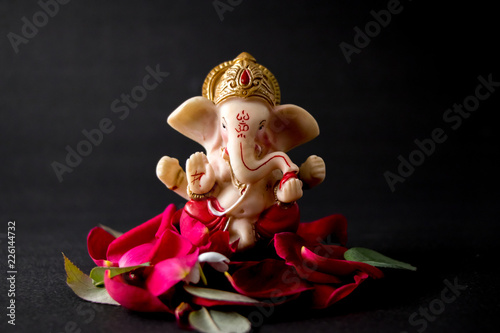 Photo Lord Ganesha Idol with rose petals, white flowers and leaves on Black background