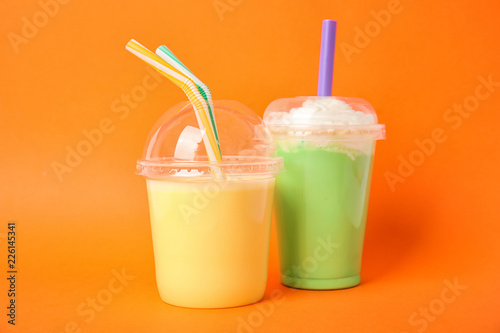 Plastic cups of tasty milk shakes on color background