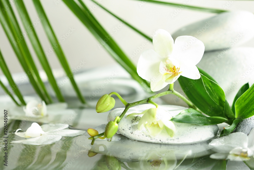 Naklejka premium Spa stones, orchid and bamboo leaves in water. Space for text