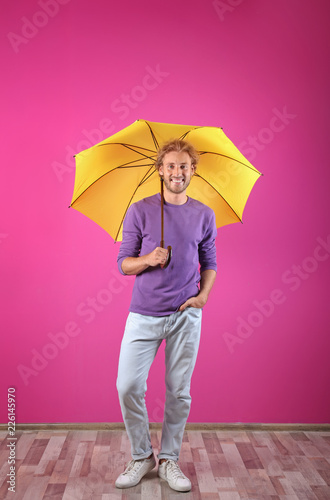 Man with yellow umbrella near color wall