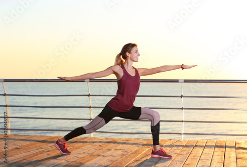 Young woman doing fitness exercises on pier in morning