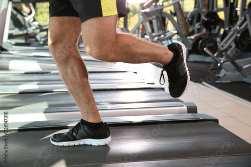 Strong young man on treadmill in gym, closeup of legs