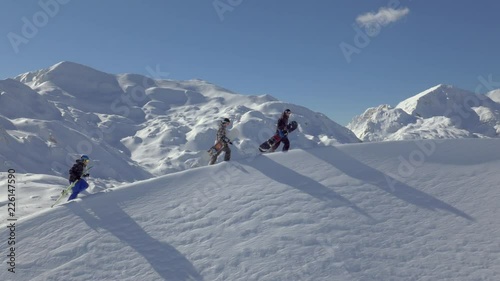 Aerial - Flyover two snowboarders and a skier walking uphill on the mountain ridge on a sunny day in winter