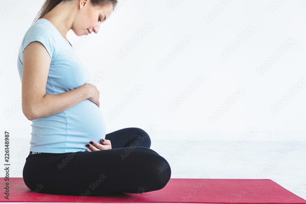 Fototapeta premium pregnancy, sport, fitness, people and healthy lifestyle concept - happy pregnant woman exercising yoga and and meditating in lotus pose in white background gym
