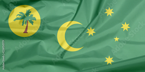 Fabric flag of Cocos (Keeling) Islands. Crease of Cocos (Keeling) Islands flag background, a palm tree on a gold disc, crescent and southern cross on green. © Achisatha