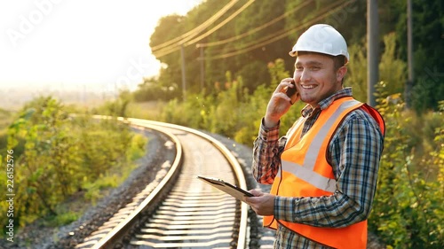 Happy railway employee with a phone and a notebook on the railroad, reports the result of the check