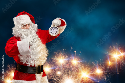 Santa Claus on a blue background points his finger at the clock. Christmas concept. photo