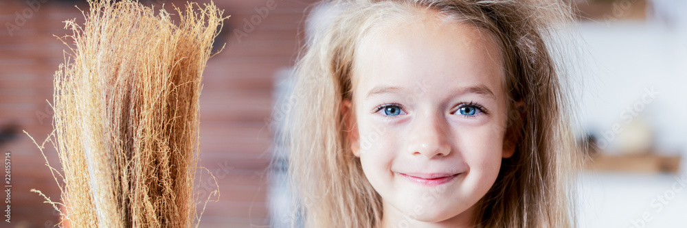 Cute little girl with messy hair, dressed up as a witch, holding a broom, looking at camera smiling. Halloween party or carnival costume banner. Cute little girl with messy hair, dressed up as a witch, holding a broom, looking at camera smiling. Halloween party or carnival costume banner.