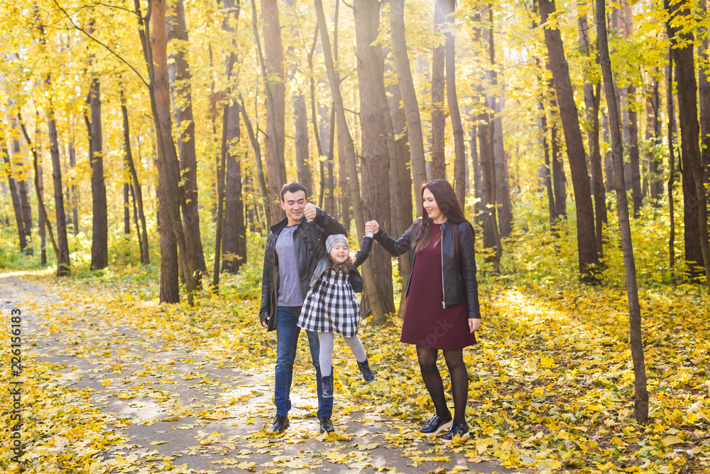 Fototapeta premium People, family and leisure concept - mixed race father and mother have fun in autumn park with their daughter