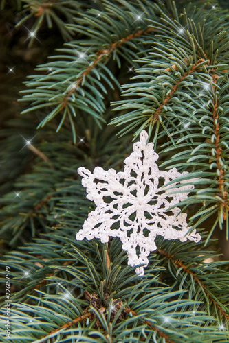White cotton crocheted snowflake on green christmas fur tree