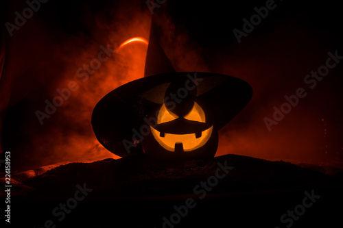 Halloween concept. Jack-o-lantern smile and scary eyes for party night. Close up view of scary pumpkin with witch hat on at dark foggy background. Selective focus.