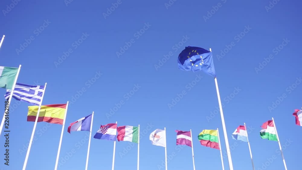 Flag of European Union with EU member flags on the background against the blue sky. Smooth slowmotion from a 120 fps original shoot