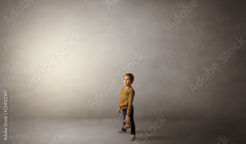 Little waggish kid staying alone in a big empty room with his plush 