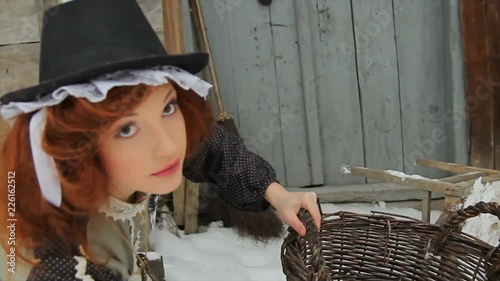 A beautiful red-haired girl in ethnic clothes is standing with a large basket on the street in winter. There is a domestic rat on the girl s hat. Fairy-tale character. Cinderella photo