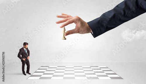 Little businessman thinking about chess strategy with a big hand concept 
