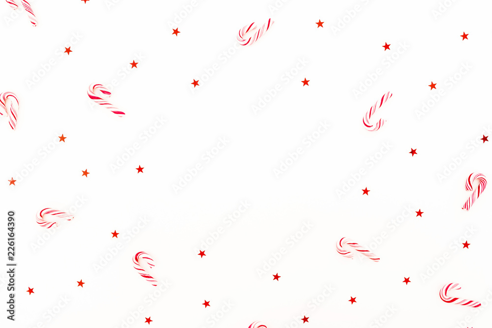 Christmas frame composition with candy cane and red shiny confetti on white background. Flat lay, top view.