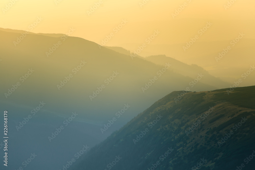 A dreamy, hazy landscape of a mountains close to sunset. Sun flas\re and misty look in blue tones. Mountain landscape in evening. Tatra mountains in Slovakia, Europe.