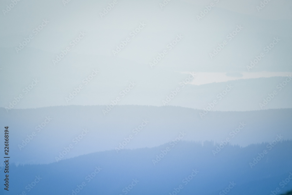 A dreamy, hazy landscape of a mountains close to sunset. Sun flas\re and misty look in blue tones. Mountain landscape in evening. Tatra mountains in Slovakia, Europe.