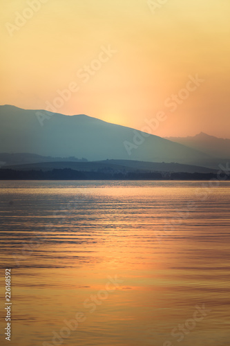 A beautiful, calm morning landscape of lake and mountains in the distance. Colorful summer scenery with mountain lake in dawn. Tatra mountains in Slovakia, Europe.