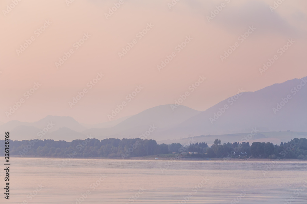 A beautiful, calm morning landscape of lake and mountains in the distance. Colorful summer scenery with mountain lake in dawn. Tatra mountains in Slovakia, Europe.