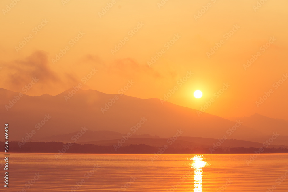 A beautiful sunrise over the lake with mountains in distance. Morning landscape in warm tones. Tatra mountains in Slovakia, Europe.