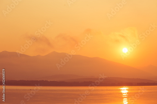 A beautiful sunrise over the lake with mountains in distance. Morning landscape in warm tones. Tatra mountains in Slovakia, Europe.