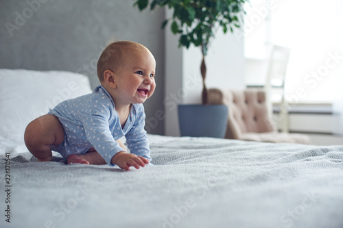 8 month old happy baby boy crawling on bed at home