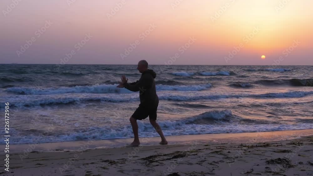 Athletic man practicing Tai Chi at sunset over the sea Athletic man practicing Tai Chi at sunset over the sea