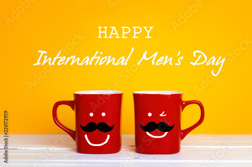 International men's day background with two red coffee mugs with a smiling whiskered faces on a yellow background.