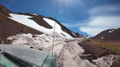 4x4 van traveling through gravel road with snow on the track. Desertic altiplane landscape of The Andes Mountains. Colored sandstone hills coverd with snow. Car's hook detail. Excursion Brava Lagoon photo