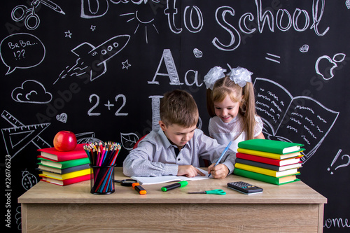 Schoolkids working at the desk with books, school supplies. Left-handed boy writing the text and smiling girl looking at the process