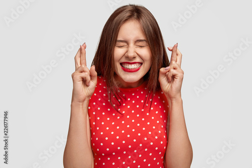 Photo Pleased attractive European woman makes wish to win, raises hands with crossed f
