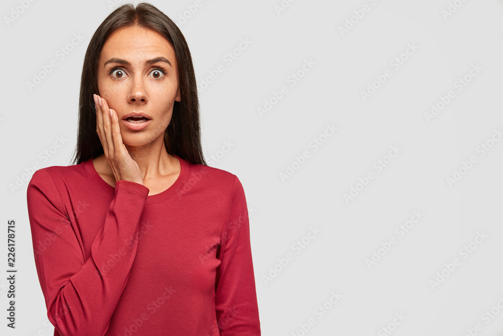 Shocked brunette woman looks with bated breath at camera, cant believe in failure, has eyes popped out, dressed in casual red sweater, isolated over white background with copy space for your promotion Shocked brunette woman looks with bated breath at camera, cant believe in failure, has eyes popped out, dressed in casual red sweater, isolated over white background with copy space for your promotion