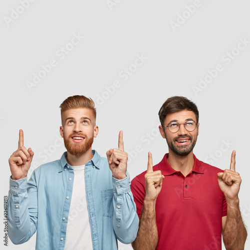 Try this. Vertical shot of satisfied two guys or fellows point upwards, suggest go upstairs, have thick beards, stand closely to each other against white background. We ned to come and look there photo