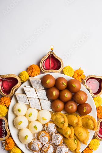 Diwali Rangoli made using Diya/oil lamp, flowers and plate full of Gulab Jamun, Rasgulla, kaju katli, morichoor / Bundi Laddu, Gujiya or Karanji  photo