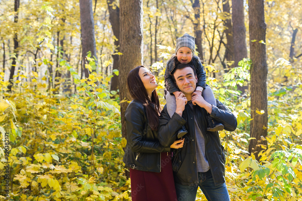 Family, autumn, people concept - young family walking in autumn park. Daughter sitting on dad's shoulders